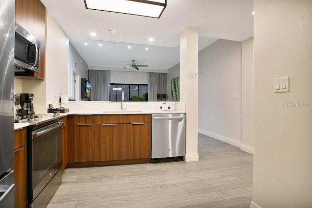 kitchen with light wood finished floors, brown cabinetry, appliances with stainless steel finishes, light countertops, and a sink