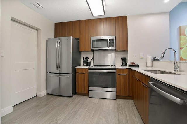 kitchen featuring a sink, light countertops, appliances with stainless steel finishes, light wood finished floors, and brown cabinetry