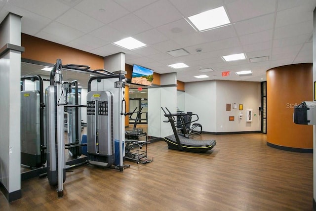 exercise room with a paneled ceiling, baseboards, and wood finished floors