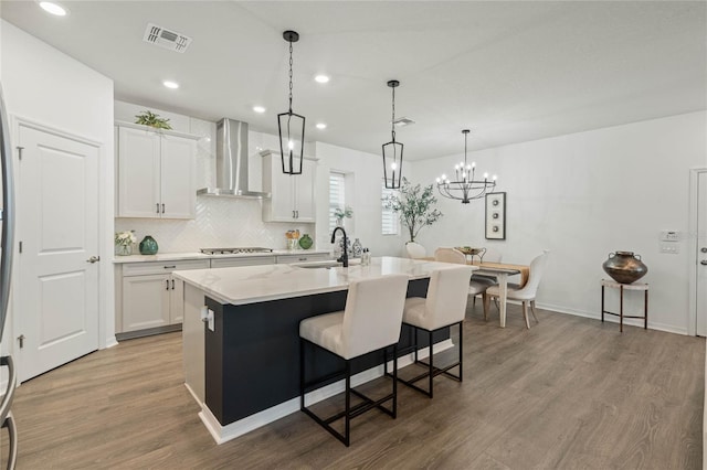 kitchen featuring wood finished floors, a kitchen island with sink, wall chimney range hood, a kitchen bar, and a sink