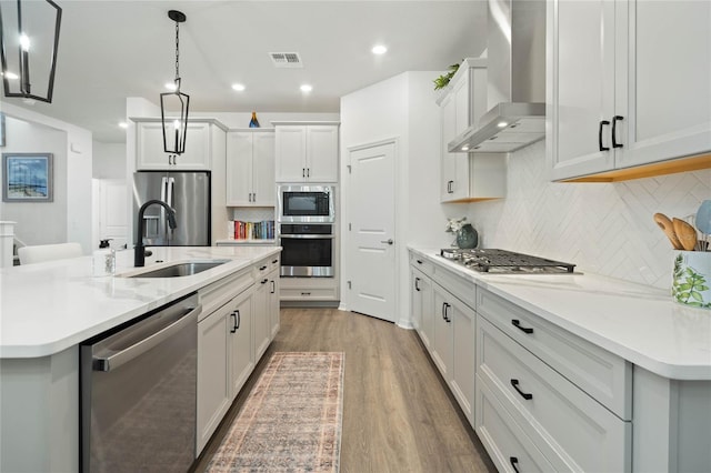 kitchen featuring stainless steel appliances, visible vents, light wood-style flooring, a sink, and wall chimney range hood