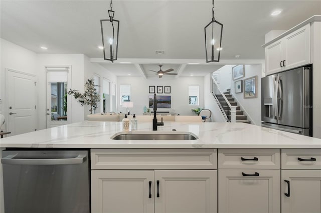 kitchen with stainless steel appliances, open floor plan, a sink, and light stone countertops