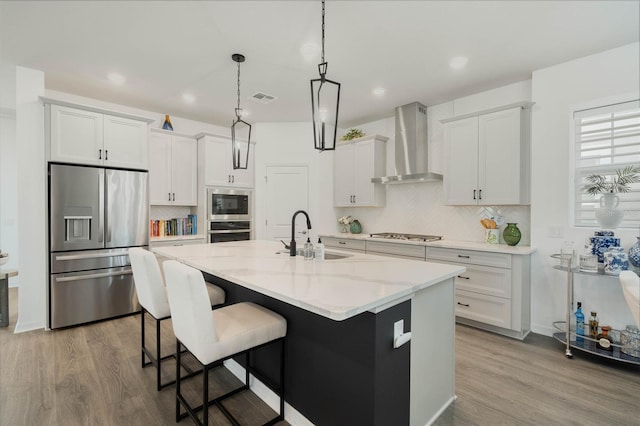 kitchen with a sink, visible vents, wall chimney range hood, appliances with stainless steel finishes, and backsplash