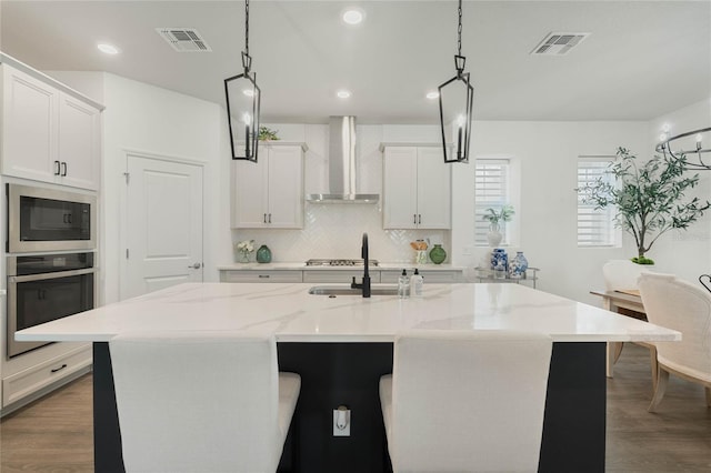 kitchen with wall chimney exhaust hood, visible vents, appliances with stainless steel finishes, and backsplash