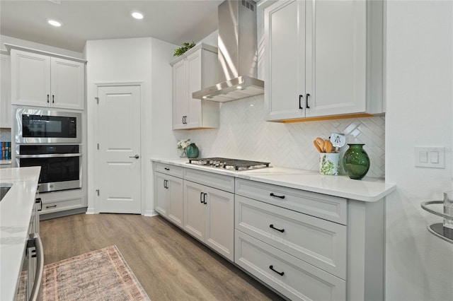 kitchen with stainless steel appliances, tasteful backsplash, wall chimney exhaust hood, and wood finished floors