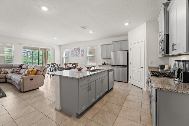kitchen with stainless steel appliances, gray cabinets, a sink, light stone countertops, and open floor plan
