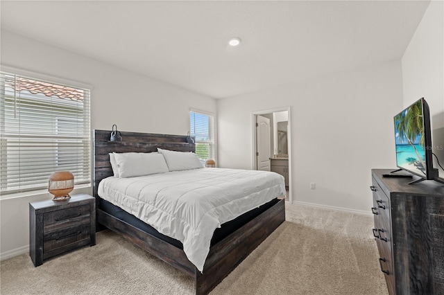 bedroom featuring ensuite bath, light carpet, and baseboards
