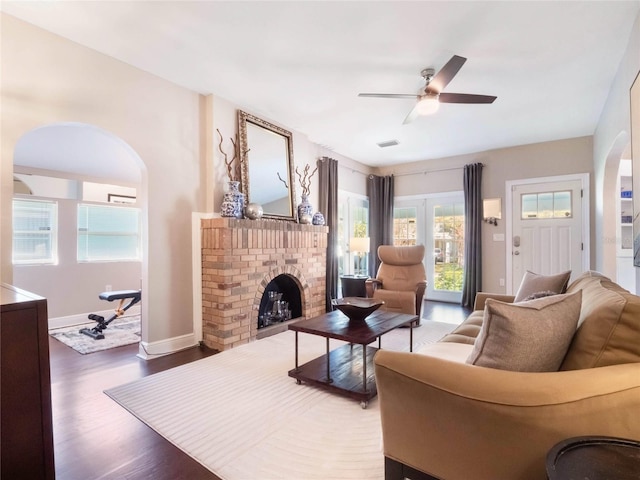 living room with baseboards, arched walkways, ceiling fan, wood finished floors, and a brick fireplace