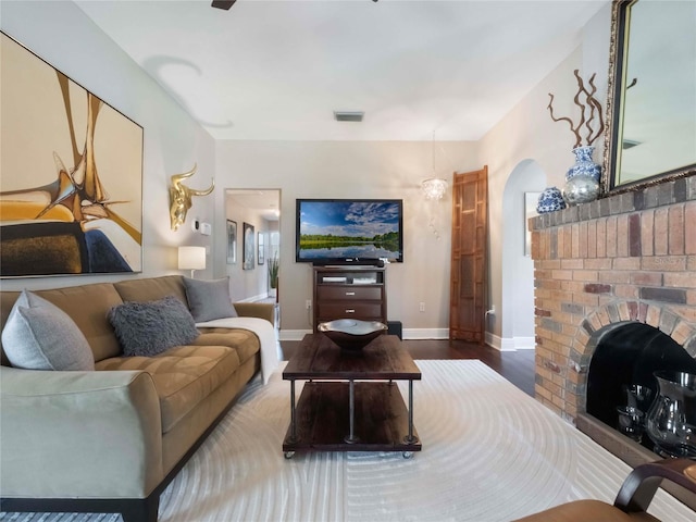 living area featuring baseboards, visible vents, arched walkways, wood finished floors, and a fireplace