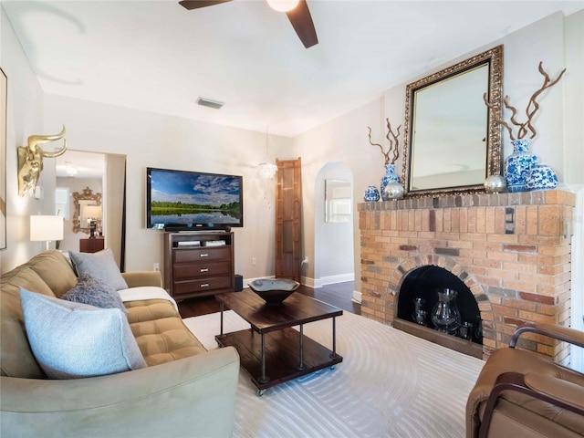 living area with arched walkways, a fireplace, visible vents, ceiling fan, and wood finished floors