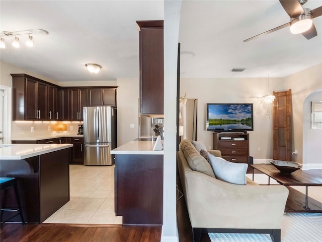 kitchen featuring freestanding refrigerator, light countertops, a kitchen breakfast bar, and dark brown cabinets