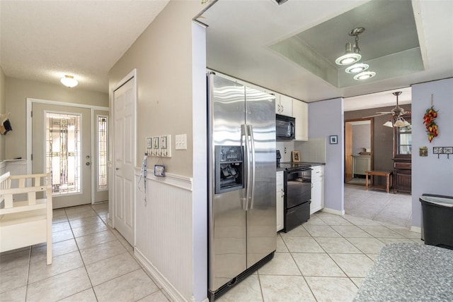 kitchen featuring light tile patterned floors, white cabinets, wainscoting, black appliances, and a tray ceiling