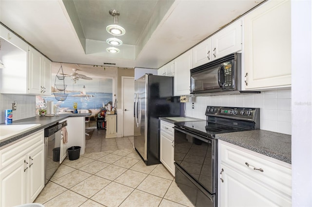 kitchen featuring dark countertops, a raised ceiling, white cabinetry, and black appliances