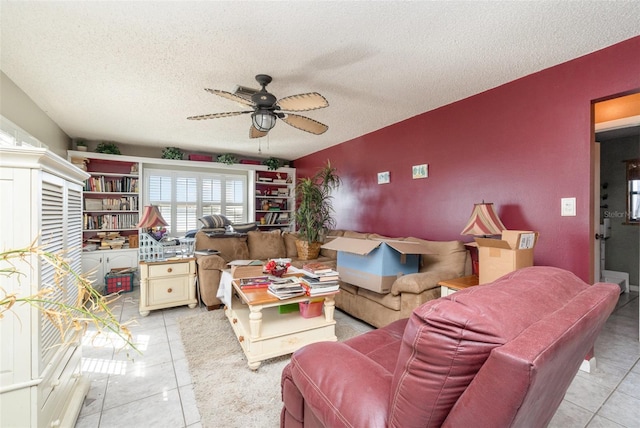 living area with a textured ceiling, an accent wall, light tile patterned floors, and a ceiling fan