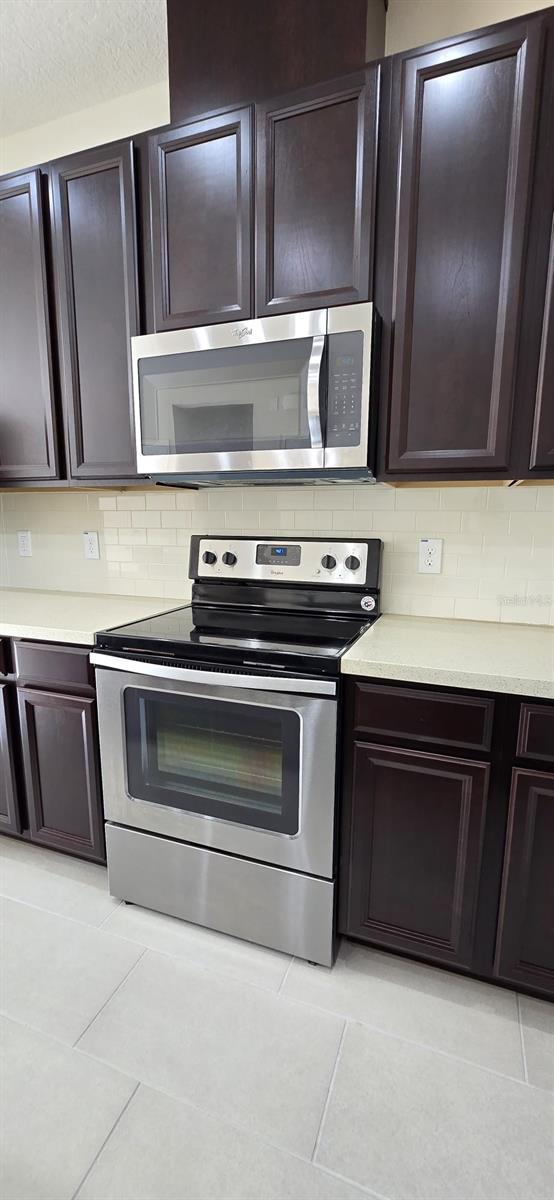 kitchen featuring appliances with stainless steel finishes, light countertops, backsplash, and dark brown cabinets