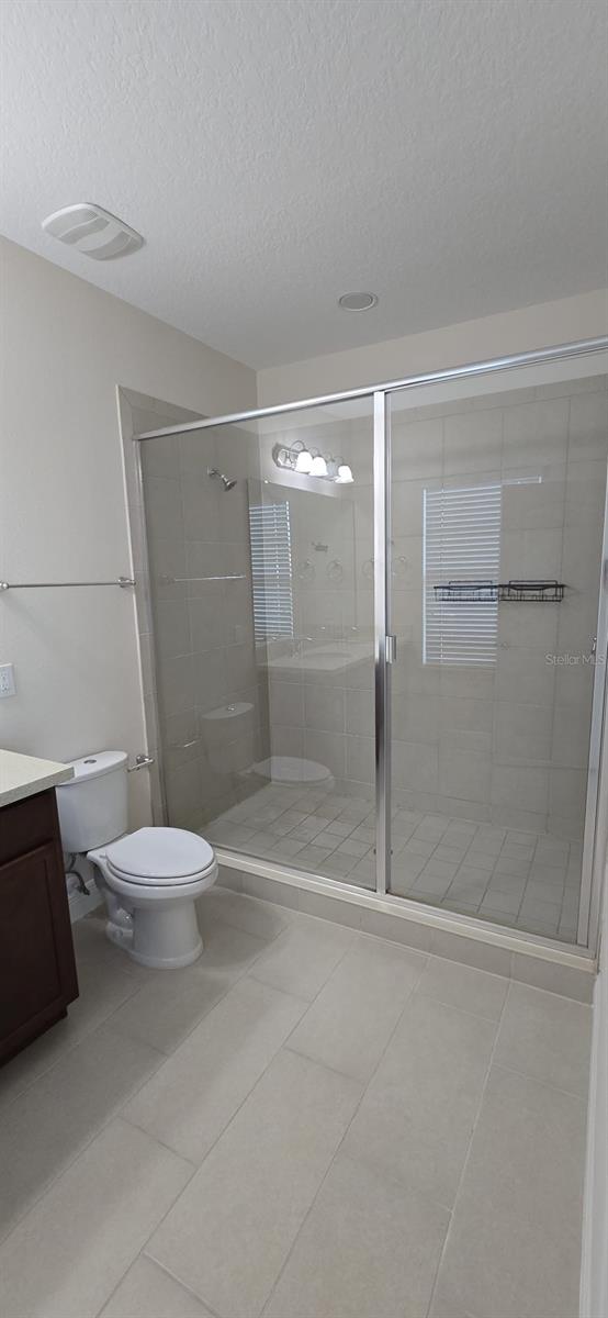 bathroom featuring toilet, tile patterned flooring, a textured ceiling, vanity, and a shower stall