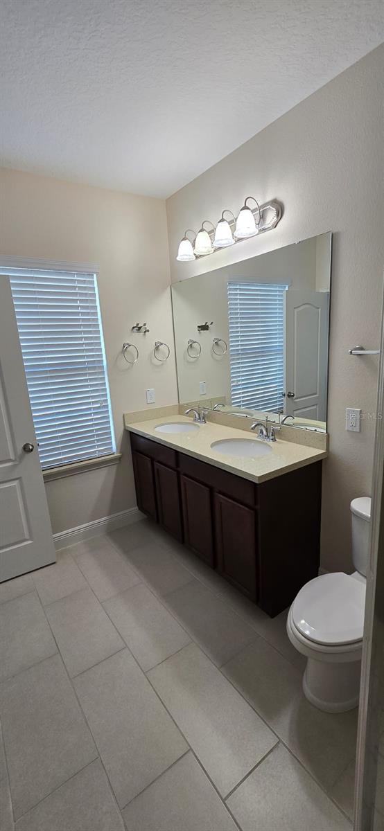 bathroom featuring tile patterned flooring, baseboards, toilet, and double vanity