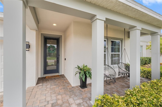 doorway to property featuring a garage, covered porch, and stucco siding