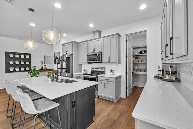 kitchen featuring dark wood-style flooring, a breakfast bar area, stainless steel appliances, gray cabinets, and a sink