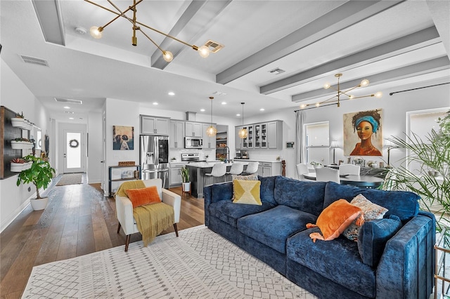 living area featuring dark wood-type flooring, beamed ceiling, visible vents, and a notable chandelier