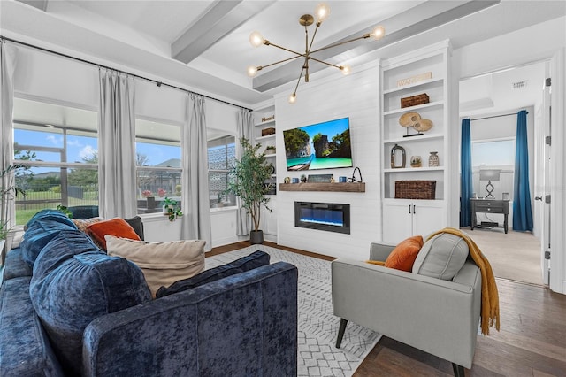 living room featuring a glass covered fireplace, wood-type flooring, beam ceiling, built in shelves, and a notable chandelier