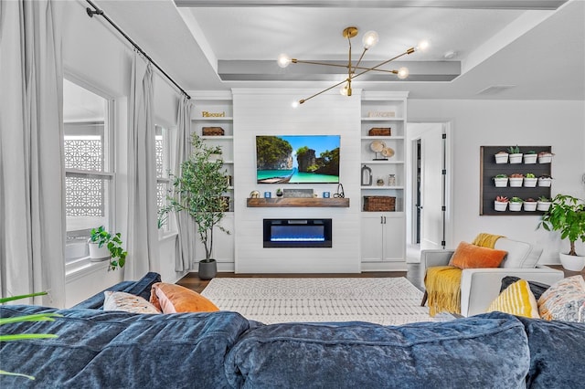 living area with a large fireplace, built in features, wood finished floors, a tray ceiling, and a notable chandelier