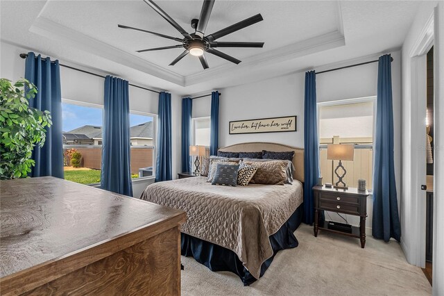 bedroom featuring a ceiling fan, a raised ceiling, crown molding, and light colored carpet