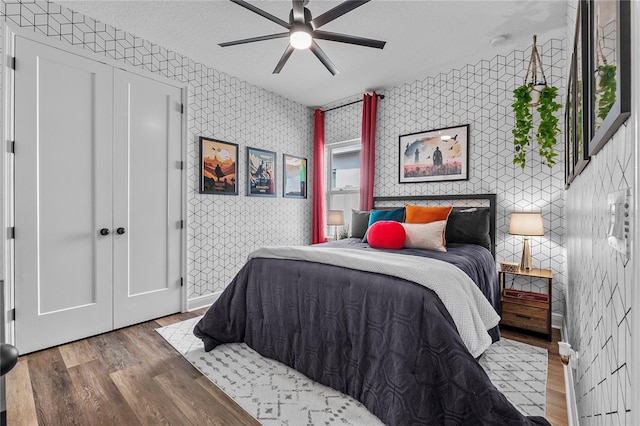 bedroom with ceiling fan, a textured ceiling, wood finished floors, baseboards, and wallpapered walls