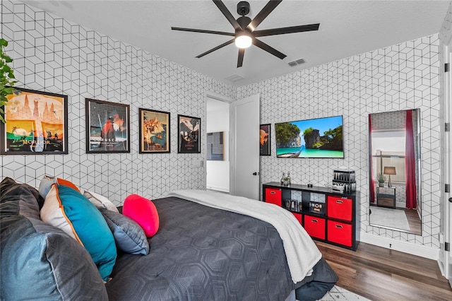 bedroom featuring ceiling fan, wood finished floors, visible vents, and wallpapered walls