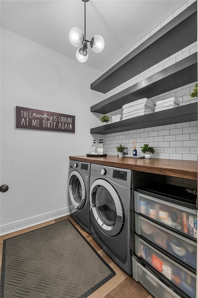 laundry area with an inviting chandelier, washing machine and dryer, wood finished floors, laundry area, and baseboards