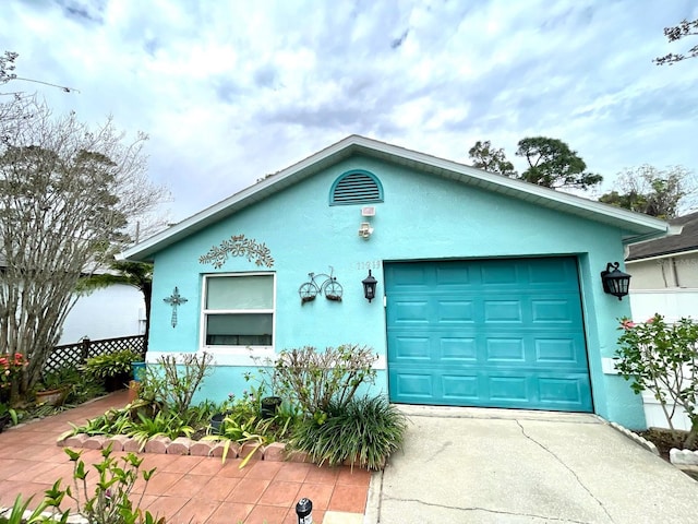 view of front of property featuring stucco siding, concrete driveway, fence, a garage, and an outdoor structure