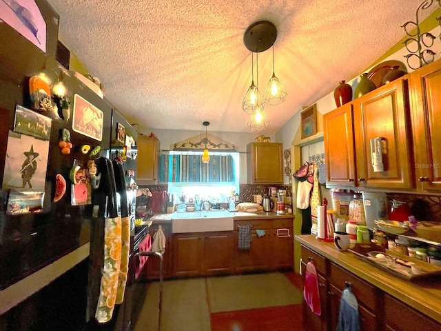 kitchen with lofted ceiling, freestanding refrigerator, hanging light fixtures, a textured ceiling, and a sink
