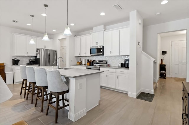 kitchen with a breakfast bar area, stainless steel appliances, a sink, visible vents, and an island with sink