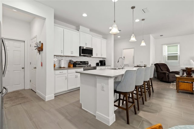 kitchen with white cabinets, decorative backsplash, a breakfast bar area, stainless steel appliances, and a sink