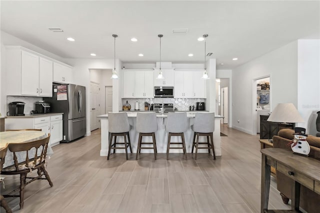 kitchen with visible vents, appliances with stainless steel finishes, a breakfast bar, light countertops, and white cabinetry