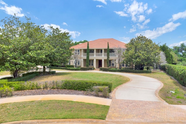 view of front of house featuring a balcony, a tiled roof, decorative driveway, and a front yard