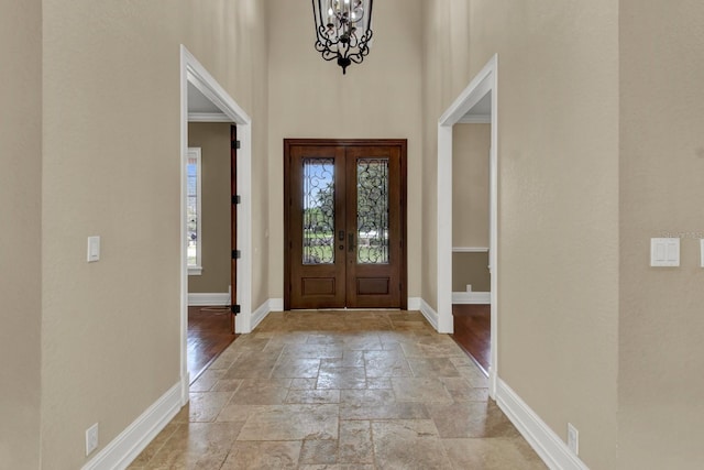 foyer entrance with a high ceiling, baseboards, a chandelier, and stone tile flooring