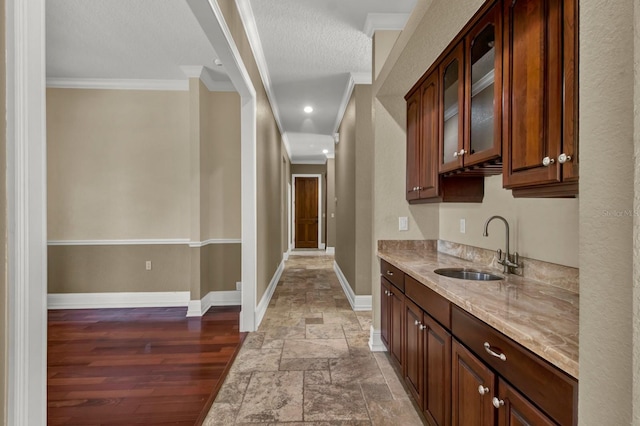 bar featuring crown molding, a sink, baseboards, and stone tile floors