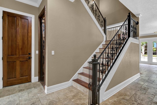 stairway with a textured ceiling, stone tile floors, baseboards, french doors, and ornamental molding