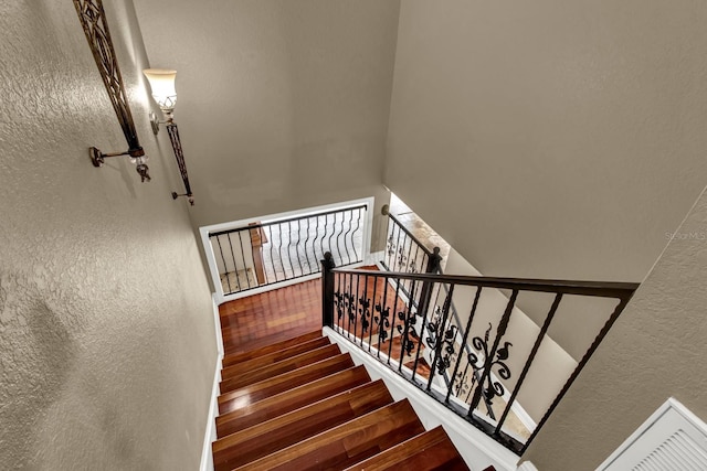 staircase with wood finished floors and a textured wall