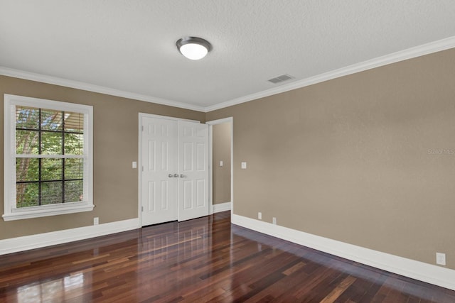 empty room featuring baseboards, visible vents, wood finished floors, and ornamental molding