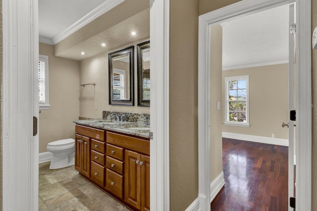 bathroom featuring double vanity, baseboards, toilet, ornamental molding, and a sink