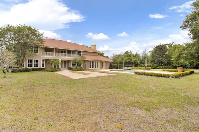 rear view of house with a patio, french doors, a lawn, an outdoor pool, and a chimney