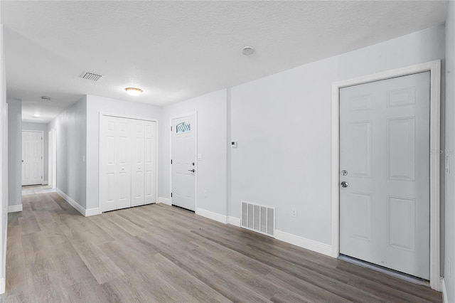 foyer with a textured ceiling, wood finished floors, visible vents, and baseboards