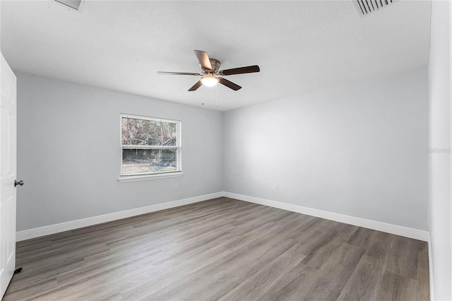 spare room featuring ceiling fan, wood finished floors, visible vents, and baseboards