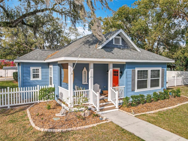 bungalow-style home featuring a porch, a shingled roof, fence, and a front yard