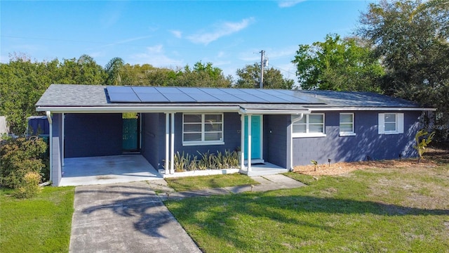 ranch-style home with concrete driveway, an attached carport, roof with shingles, roof mounted solar panels, and a front lawn