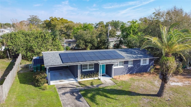 ranch-style house featuring an attached carport, fence, driveway, roof mounted solar panels, and a front lawn