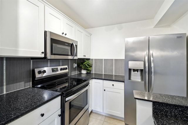 kitchen with light tile patterned flooring, white cabinets, appliances with stainless steel finishes, backsplash, and dark stone countertops