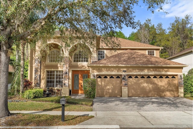 view of front of home with a garage, stone siding, roof with shingles, decorative driveway, and stucco siding